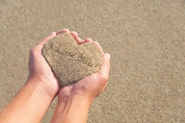 Händer som håller en sand i form av hjärta med texten "i love you" — Stockfoto