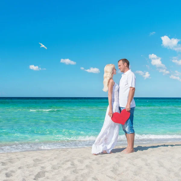 Liebespaar am sonnigen Meeresstrand mit rotem Herz — Stockfoto