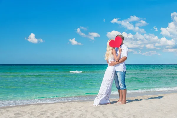 Älskande par på soliga stranden med rött hjärta — Stockfoto