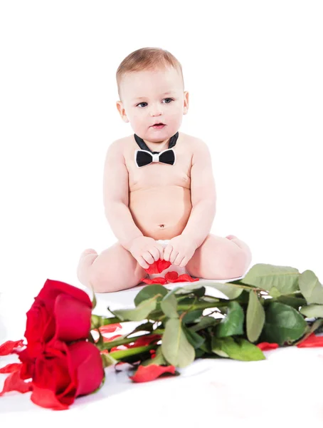 Niedlicher Säugling in Fliege mit roten Rosen und Blütenblättern — Stockfoto