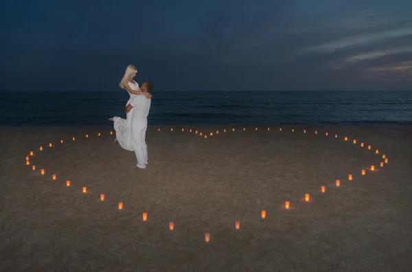 Pareja joven en velas corazón en la playa del mar contra el atardecer — Foto de Stock