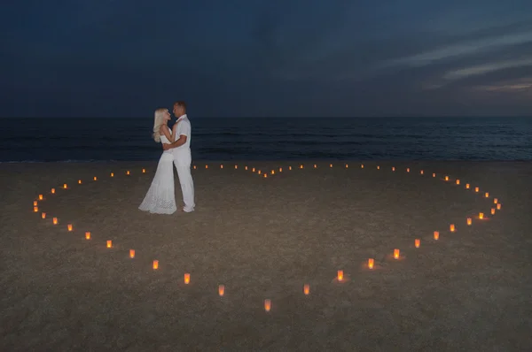 Jovem casal em velas coração na praia do mar contra o pôr do sol — Fotografia de Stock