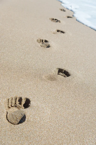Pegadas na areia da praia do mar com espuma de onda — Fotografia de Stock
