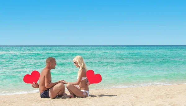 Älskande par på sandig strand med röda hjärtan — Stockfoto