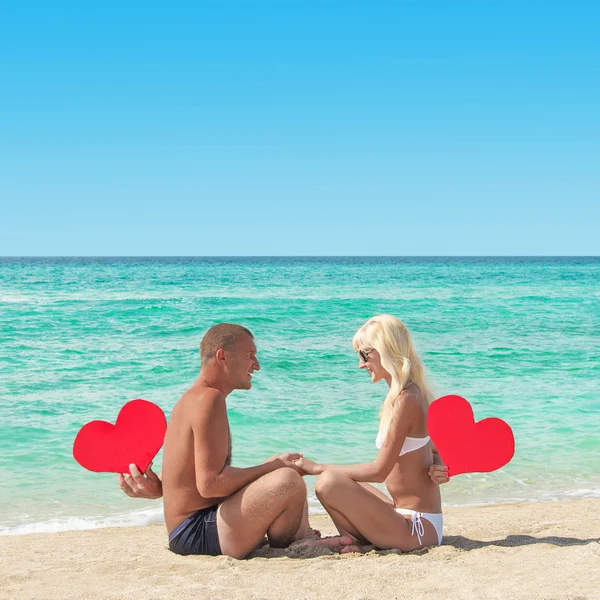 Pareja cariñosa en la playa de arena con corazones rojos —  Fotos de Stock