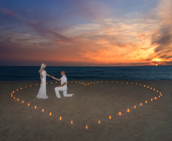 Pareja joven en velas corazón en la playa del mar contra el atardecer — Foto de Stock