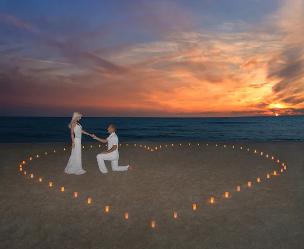 Pareja joven en velas corazón en la playa del mar contra el atardecer — Foto de Stock