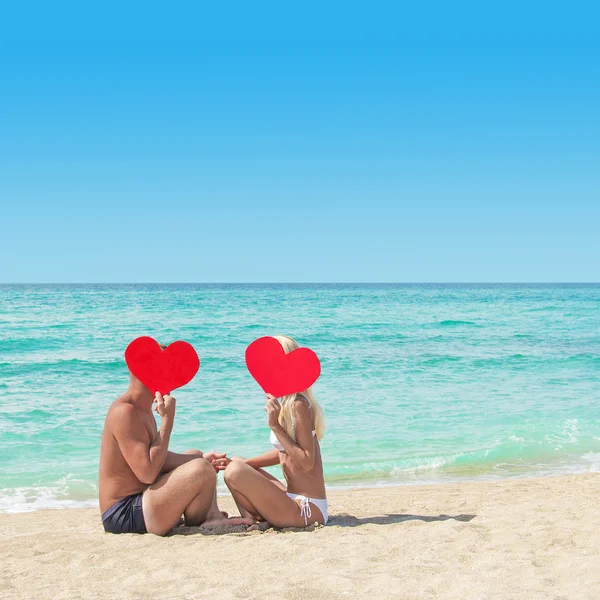 Älskande par på sandig strand med röda hjärtan — Stockfoto