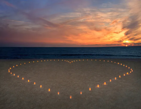 Corazón de velas en la playa de arena de mar contra la puesta de sol brillante —  Fotos de Stock