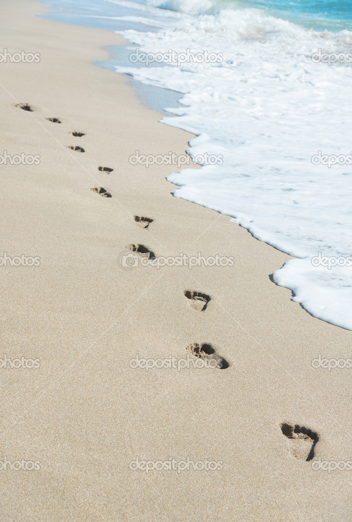 Footprints on sea beach sand with wave foam