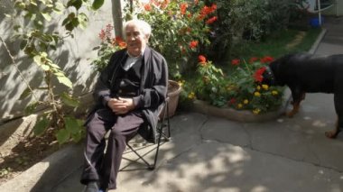 Bahçesinde yaşlı bir adam oturuyor, yanında bir Rottweiler 'la..