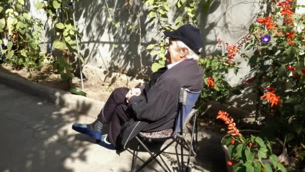 Ein älterer Mann sitzt auf einem alten Klappstuhl in seinem Hof. — Stockvideo