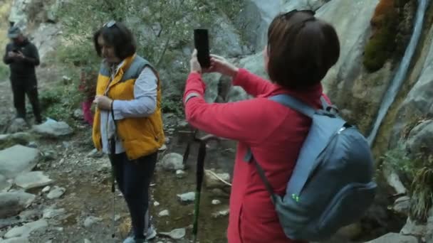 Две женщины фотографируют телефон у маленького горного водопада. — стоковое видео