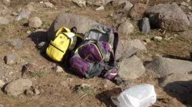 Kayaların yanında yerde turist sırt çantaları var..