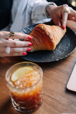 Genç bir kadın kruvasan yiyor ve kahve içiyor.