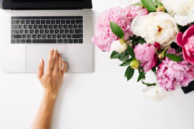 Boş ekran ve beyaz arkaplanda şakayık çiçekleri olan dizüstü bilgisayar kullanan kadın