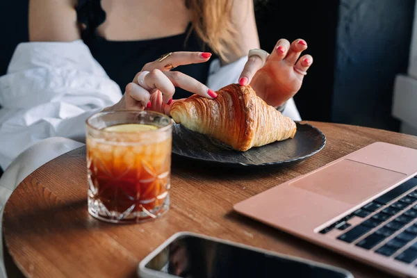 Genç bir kadın kruvasan yiyor ve kahve içiyor.
