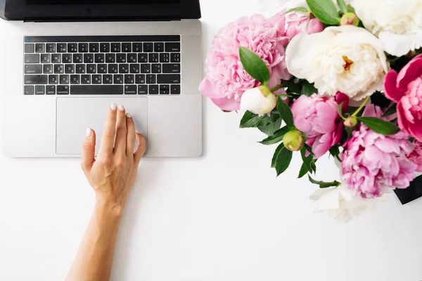 Boş ekran ve beyaz arkaplanda şakayık çiçekleri olan dizüstü bilgisayar kullanan kadın