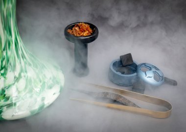 Şık yeşil nargile, siyah nargile kasesi, gri masada aromatik tütün ve sigara içilen aksesuarlar. Nargile, nargile tüttürüyor. Nargile kasesi ve hindistan cevizi kömürü.