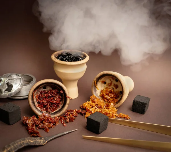 Three hookah bowls with aromatic tobacco on a brown table with smoking accessories. Hookah smoking in a hookah lounge. Red, yellow, black tobacco for hookah, charcoal, tongs