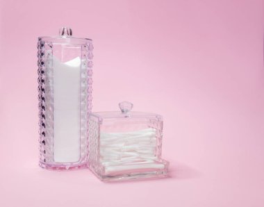 Beyaz pamuk karesi seğirme için konteynır ve açık pembe arka planda pamuk tomurcukları. Kulak, kozmetik, makyaj ve hijyen için pamuk çubuğu.