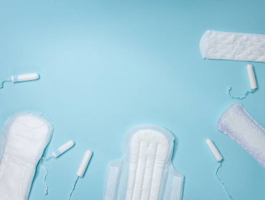 Açık mavi arka planda bir sürü beyaz tampon ve hijyenik ped bulunur. Adet döngüsü ve hamilelik. Negatif hamilelik testi ve doğum kontrol hapları.