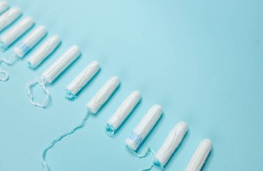 Birçok hijyenik tampon açık mavi arka planda bir sırada yatar. Adet döngüsü ve hamilelik. Negatif hamilelik testi ve doğum kontrol hapları.