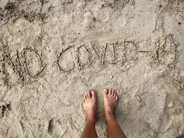 ビーチで砂の中に書かれた旅行のCovid19と足 — ストック写真