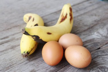 Muz ve kahverengi ahşap arka planda taze yumurta.