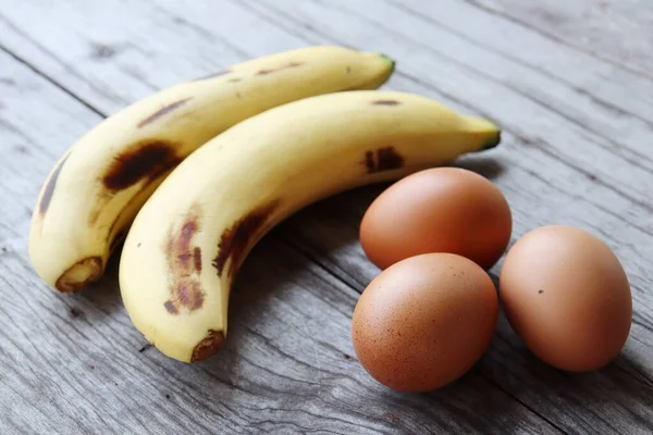 茶色の木の背景にバナナと新鮮な卵 — ストック写真