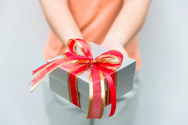Hand give silver gift box with red ribbon — Stock Photo, Image
