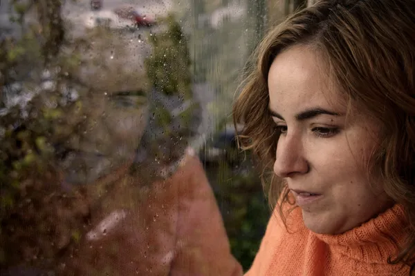 Portrait d'une femme regardant par la fenêtre un jour de pluie dans — Photo