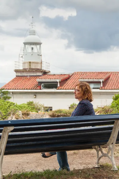 Vrouw zitten op de Bank voor de vuurtoren — Stockfoto