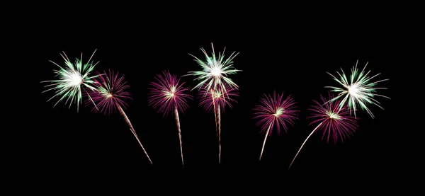 Pink and green fireworks exploding on night sky background