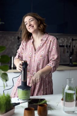 Yeşil buğday çimi suyu hazırlayan genç bir kadın dans ederken eğleniyor. Sağlıklı antioksidan içeceği.