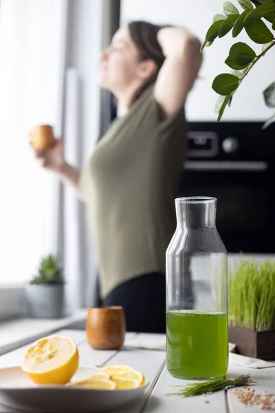 Wheatgrass juice made of fresh grass. Antioxidant energetic morning drink and young healthy woman