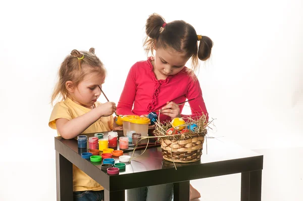 Dos niñas pequeñas para pintar huevos de Pascua sobre un fondo blanco — Foto de Stock