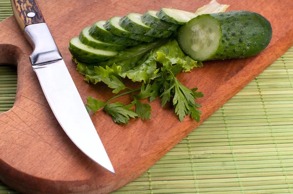 Three cucumbers and the knife on carving board. White background. Studio shot. — Stock Photo, Image