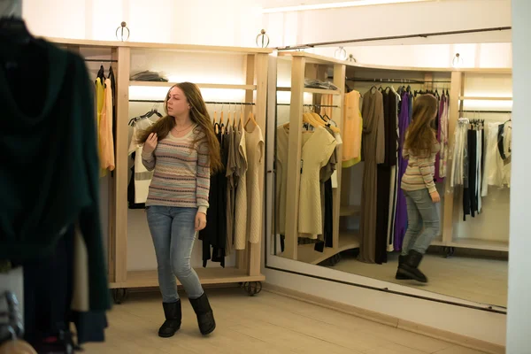 Mulher compras escolhendo vestidos olhando no espelho incerto — Fotografia de Stock