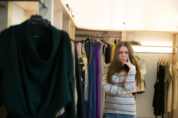 Mujer de compras elegir vestidos mirando en el espejo incierto —  Fotos de Stock