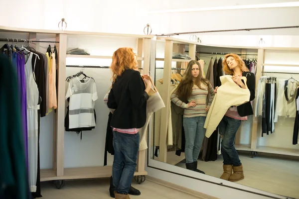 Mulher compras escolhendo vestidos olhando no espelho incerto — Fotografia de Stock