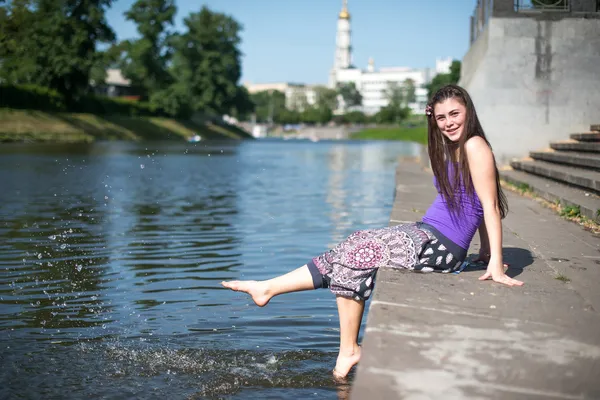 Girl sitting at the pier and hanging bare feet — Stock Photo, Image