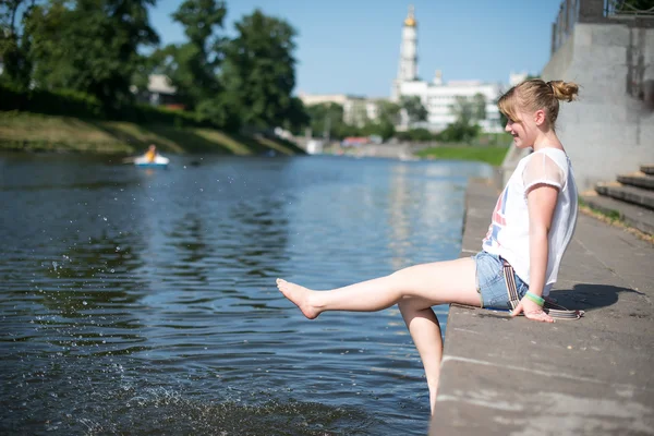 女孩坐在码头和挂赤裸的双脚 — 图库照片