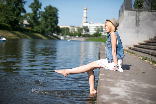 Dívka sedí u mola a visí bosé nohy — Stock fotografie