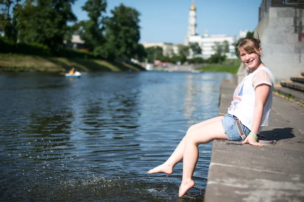 Chica sentada en el muelle y colgando los pies desnudos — Foto de Stock