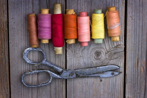 Colorful threads and old scissors on the old wooden table — Stock Photo, Image