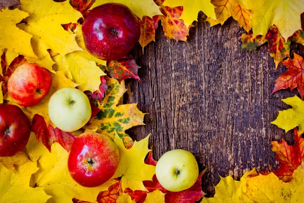 Äpfel und umgefallenes Laub auf altem Holztisch — Stockfoto