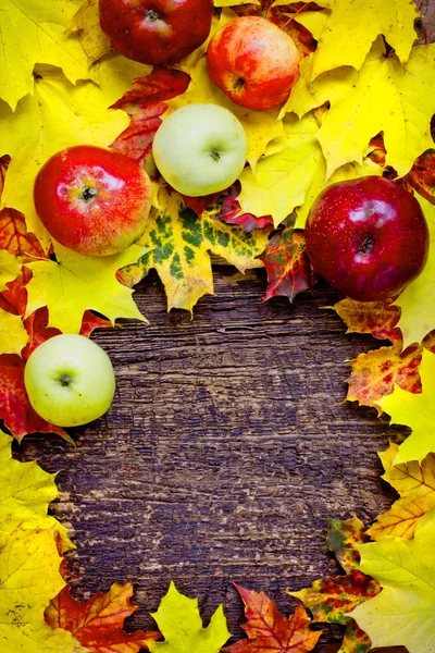 Apples and fallen leaves on old wooden table — Stock Photo, Image