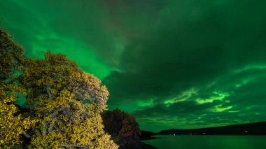 Aurora Borealis gölün yakınındaki bulutların üzerinde parlıyor.
