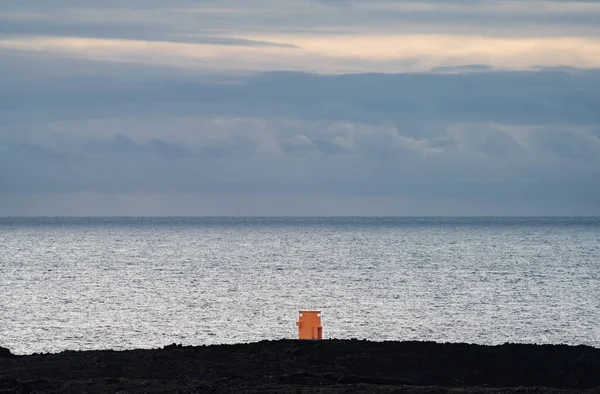 Faro naranja minúsculo frente al enorme océano — Foto de Stock